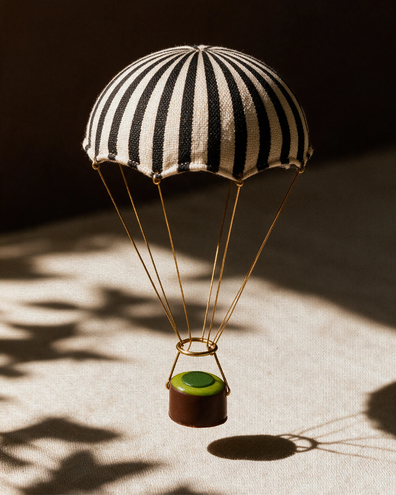 A striped miniature balloon suspending a green-topped chocolate in sunlight